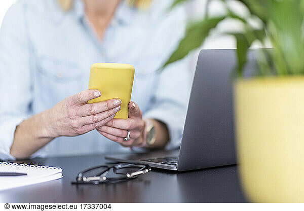 Woman using mobile phone near laptop on table at home