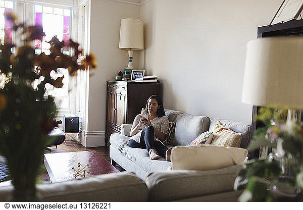Woman using mobile phone while relaxing on sofa at home