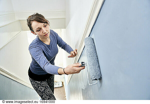 Woman using paint roller to paint staircase