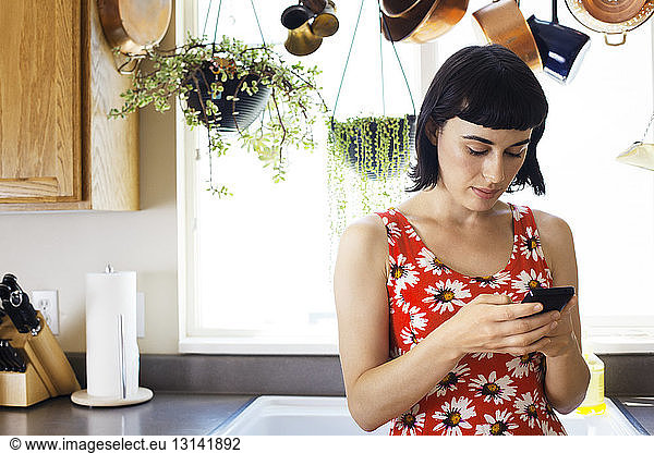 Woman using phone while leaning on kitchen counter at home