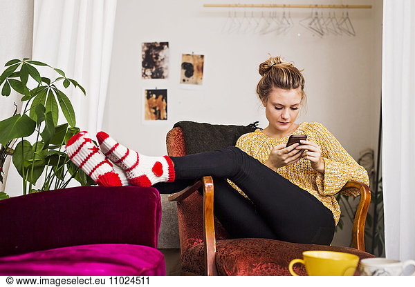 Woman using phone while resting on chair at home