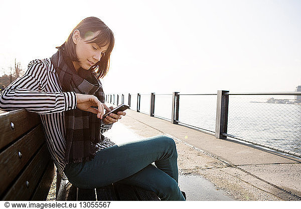 Woman using phone while sitting on bench