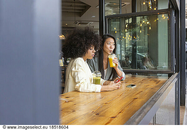 Woman using smart phone by friend drinking juice at cafe