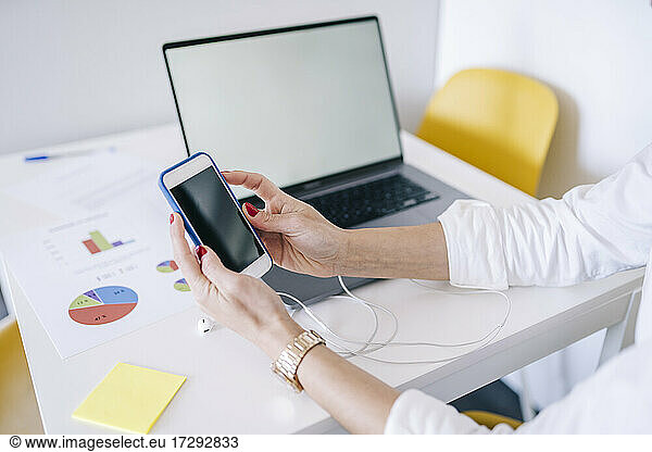 Woman using smart phone by laptop at home office