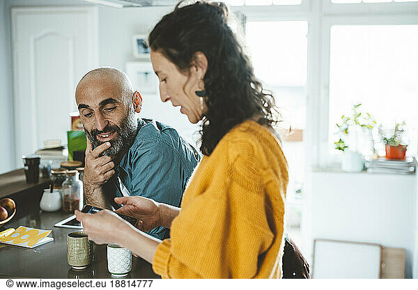 Woman using smart phone by man with hand on chin at home