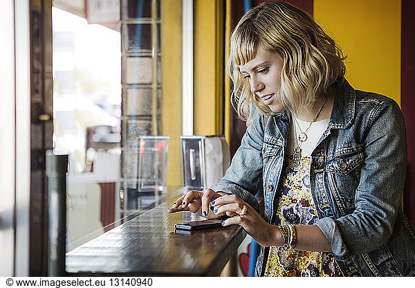 Woman using smart phone by window in cafe