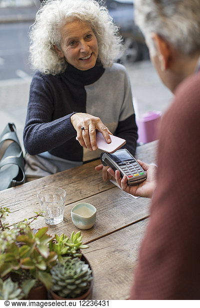 Woman using smart phone contactless payment at cafe