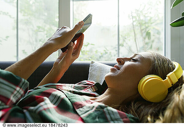 Woman using smart phone listening to music through headphones at home