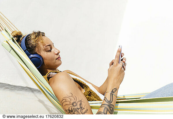 Woman using smart phone relaxing on hammock