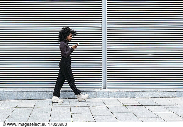 Woman using smart phone walking by wall