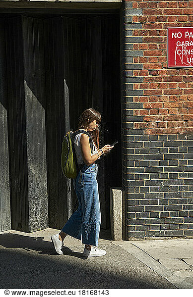 Woman using smart phone walking on footpath