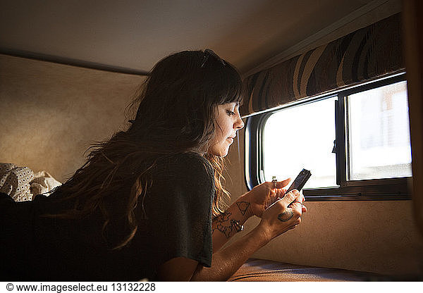Woman using smart phone while relaxing on bed in camper van