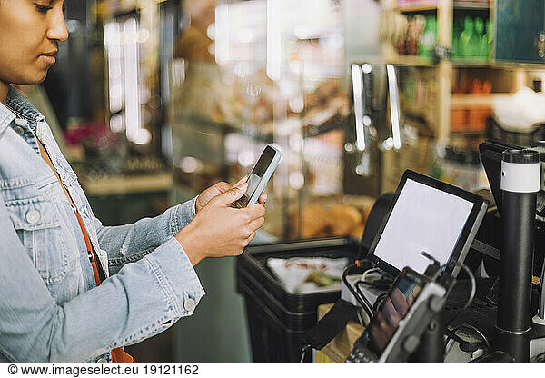 Woman using smart phone while scanning QR code for payment at store checkout