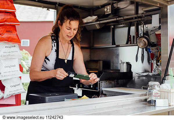 Woman using smartphone card reader for payment at food stall trailer
