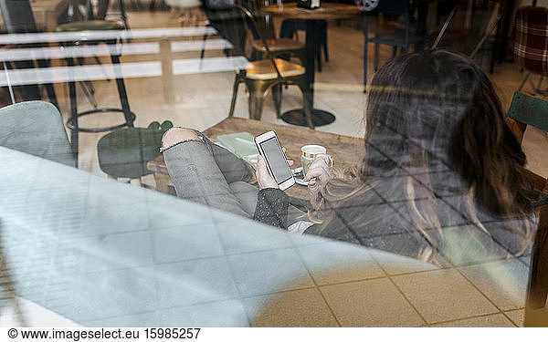 Woman using smartphone in coffee shop  seen through windowpane
