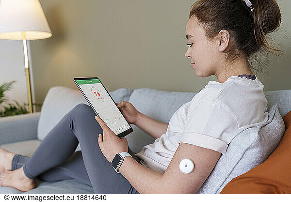 Woman using tablet PC with diabetes glucose sensor on arm at home