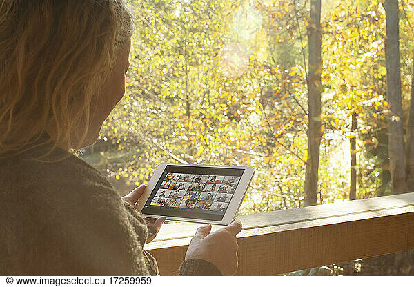 Woman video chatting with friends on digital tablet at autumn window
