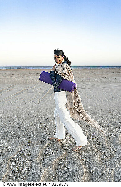 Woman walking barefooted carrying a mat while looking at camera