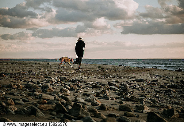 woman walking dog on the beach at sunset