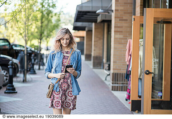Woman walking down street in front of shop texting on phone