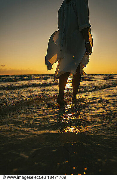 Woman walking in sea on beach at sunrise