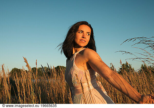 woman walking in the grass in a beautiful dress at sunset