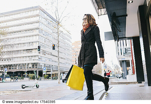 Woman walking out of store holding shopping bags in city
