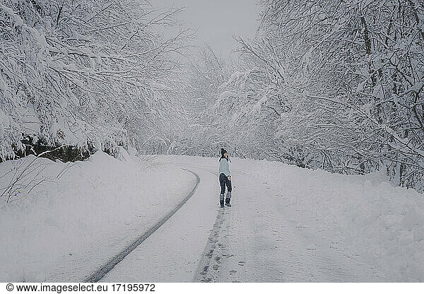 woman walking over snowy road in the forest