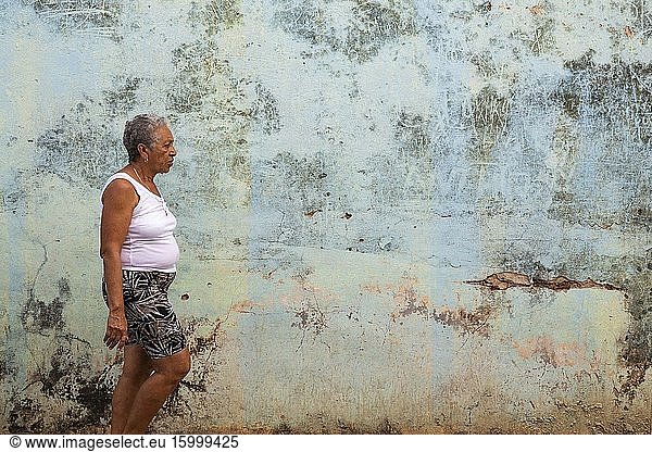 Woman walking past a decayed wall of crumbling plaster. Trinidad  Cuba.