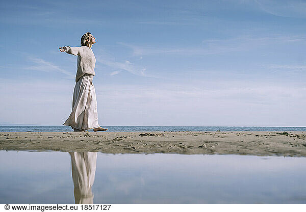 Woman walking with arms outstretched at beach