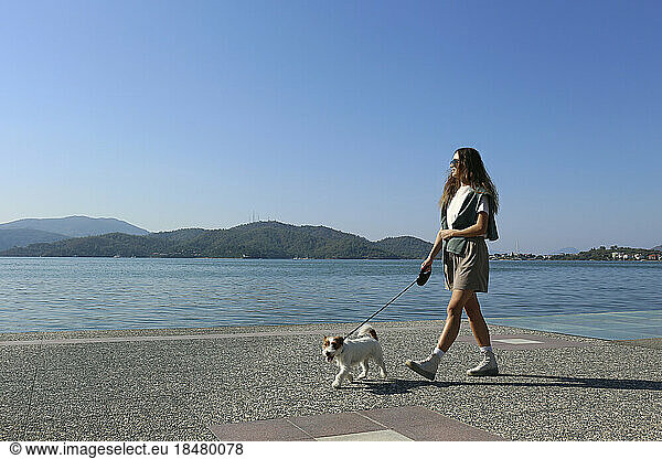 Woman walking with dog at promenade on sunny day