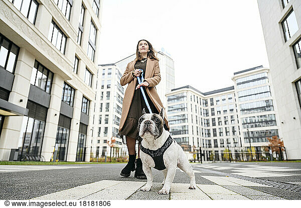 Woman walking with French bulldog in front of buildings
