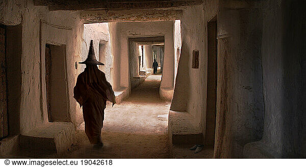 woman walking with traditional straw hat in an alley in Sanaa.
