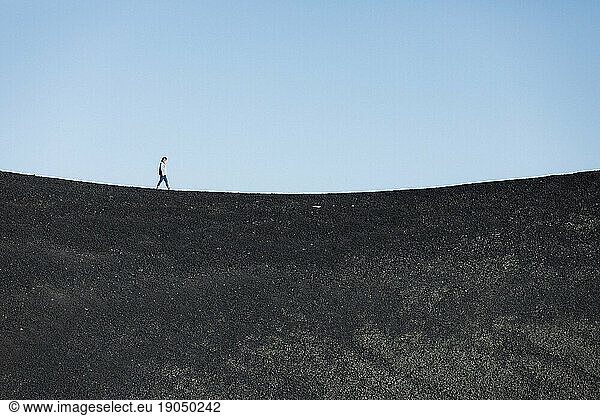 woman walks alone on a black basalt sand concave horizon line