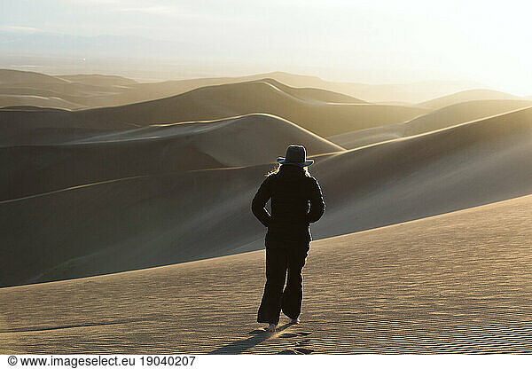 woman walks into sunset of desert dunes to explore