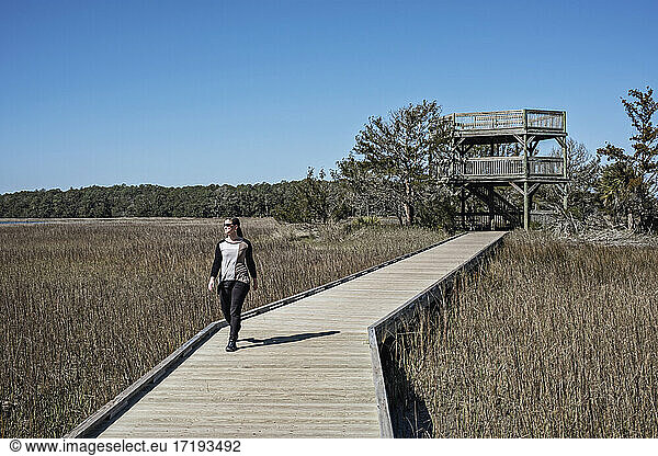 woman walks on boardwalk with observation tower  Skidaway Island  GA
