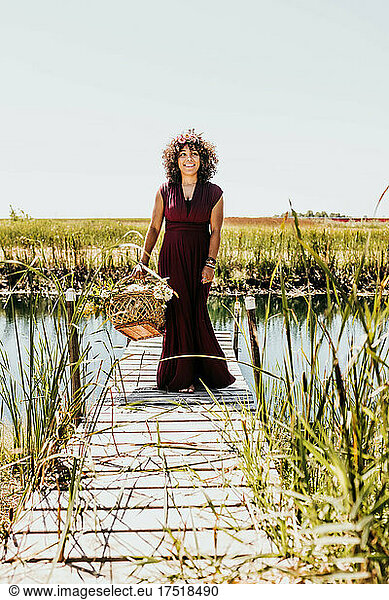 Woman walks on dock while holding woven basket full of flowers
