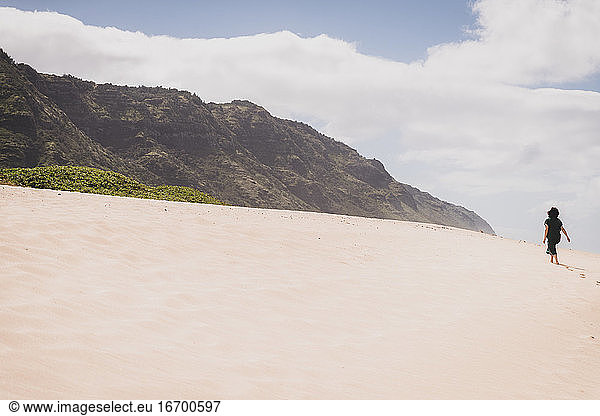 Woman walks up sandy hill towards mountains in Hawaii