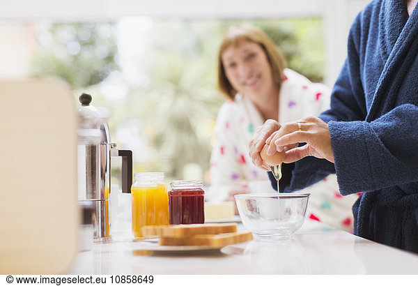 Woman watching husband crack egg in kitchen