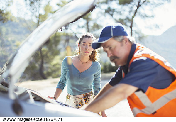 Woman watching roadside mechanic check car engine