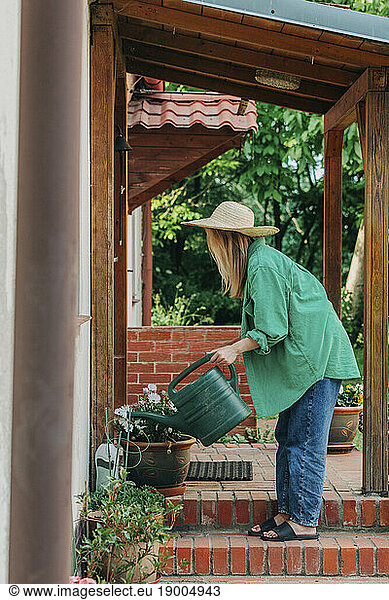 Woman watering plants outside house