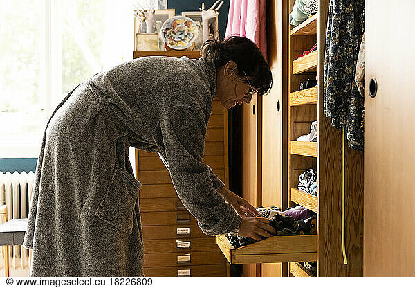 Woman wearing bathrobe searching in wardrobe drawer at home