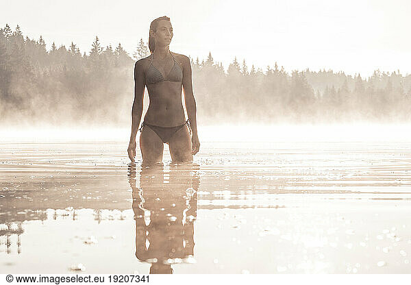 Woman wearing bikini bathing in a lake at morning mist