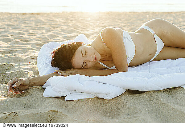 Woman wearing bikini lying on blanket at beach