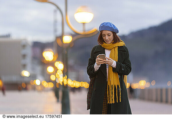 Woman wearing blue beret using mobile phone at dusk