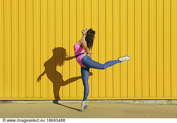 Woman wearing bodysuit showing ballet moves in front of yellow wall