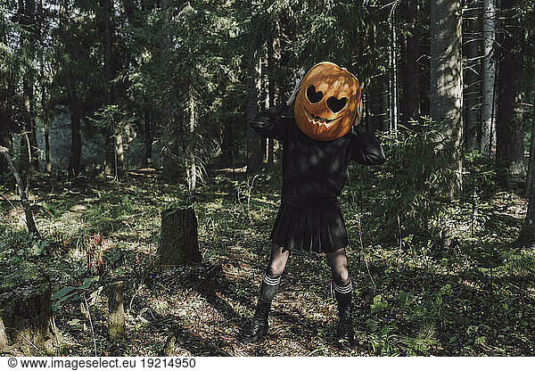Woman wearing carved Jack O' Lantern and standing in forest