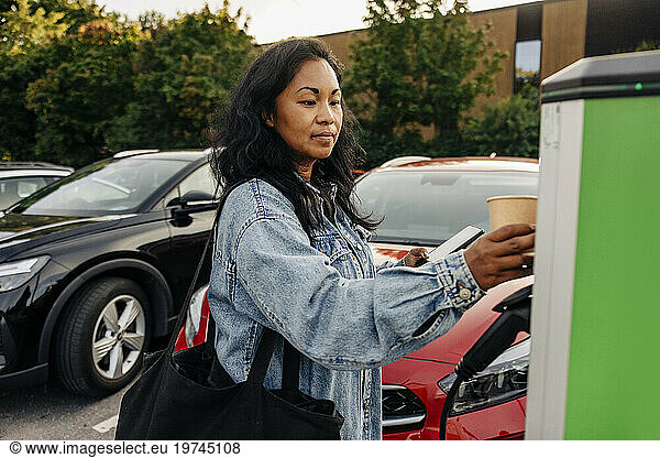 Woman wearing denim jacket operating kiosk at charging station