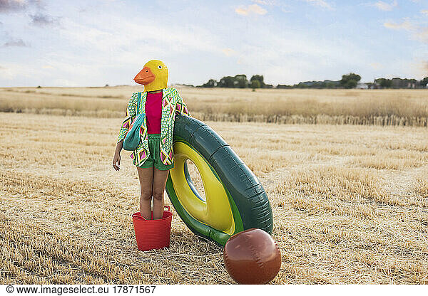 Woman wearing duck mask standing in bucket with inflatable ring at field