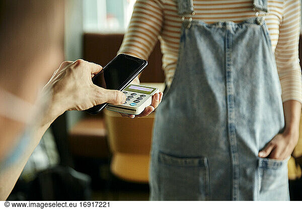 Woman wearing face mask holding contactless payment device  customer paying using a mobile phone